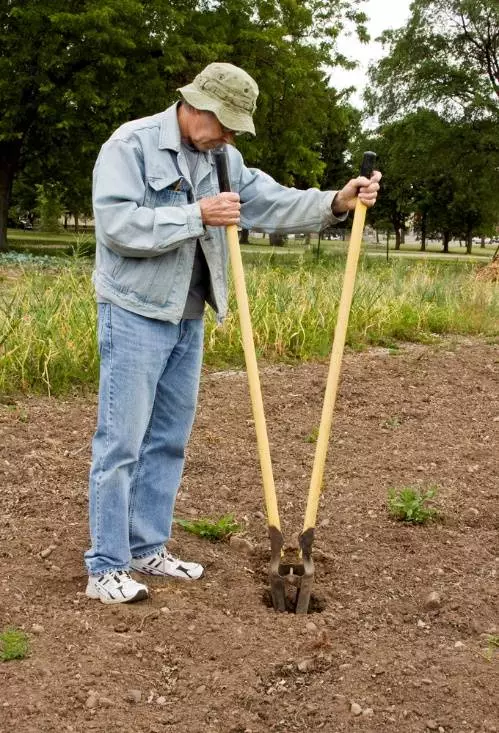 Landowner digging a hole with a post hole shovel.