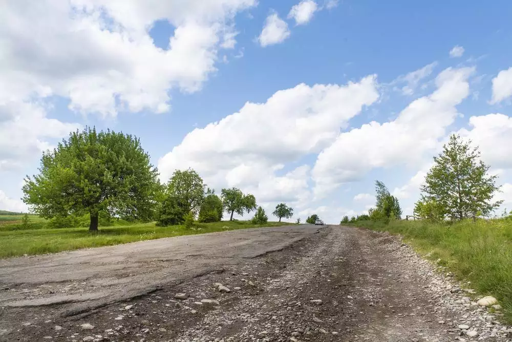 Poorly maintained paved road with asphalt crumbling to travel to homestead property.